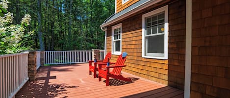 A wooden deck with two red Adirondack chairs and a stone pillar.