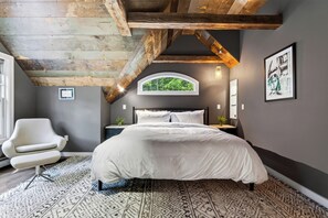 A bedroom with a large bed, a chair, a nightstand, a window with a view of trees, and a framed picture on the wall. - Timber-Frame Retreat + Chef's Kitchen + Game Room | 3.5 Acres | Bow & Beam (Sheffield)