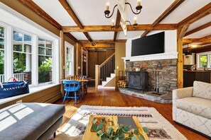 A spacious living room with a fireplace, wooden beams, a dining area, and a view of the outdoors. - Timber-Frame Retreat + Chef's Kitchen + Game Room | 3.5 Acres | Bow & Beam (Sheffield)