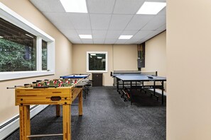 A room with a foosball table, ping pong table, and a window with a view of trees. - Timber-Frame Retreat + Chef's Kitchen + Game Room | 3.5 Acres | Bow & Beam (Sheffield)
