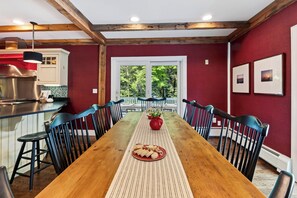 A dining area with a long wooden table, black chairs, a red vase with flowers, and a view of greenery through a window. - Timber-Frame Retreat + Chef's Kitchen + Game Room | 3.5 Acres | Bow & Beam (Sheffield)