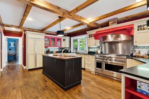 A kitchen with wooden beams, a central island, stainless steel appliances, and a red backsplash.