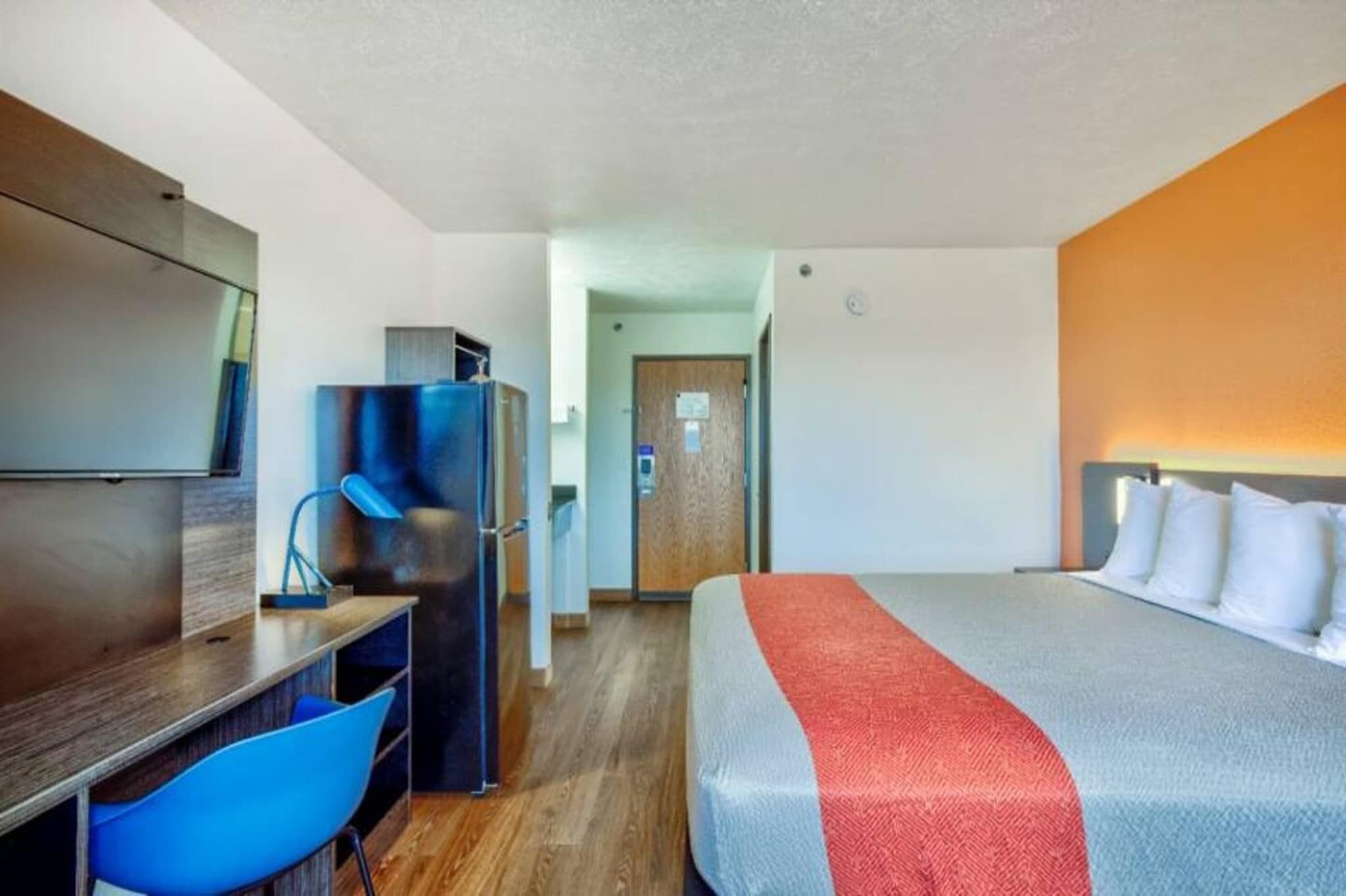 Ett hotellrum med en säng, ett skrivbord, en stol, ett kylskåp och en tv.
