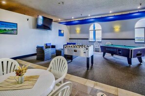 Ein Zimmer mit Billardtisch, Kicker und einem Tisch mit Stühlen und Blumen.
