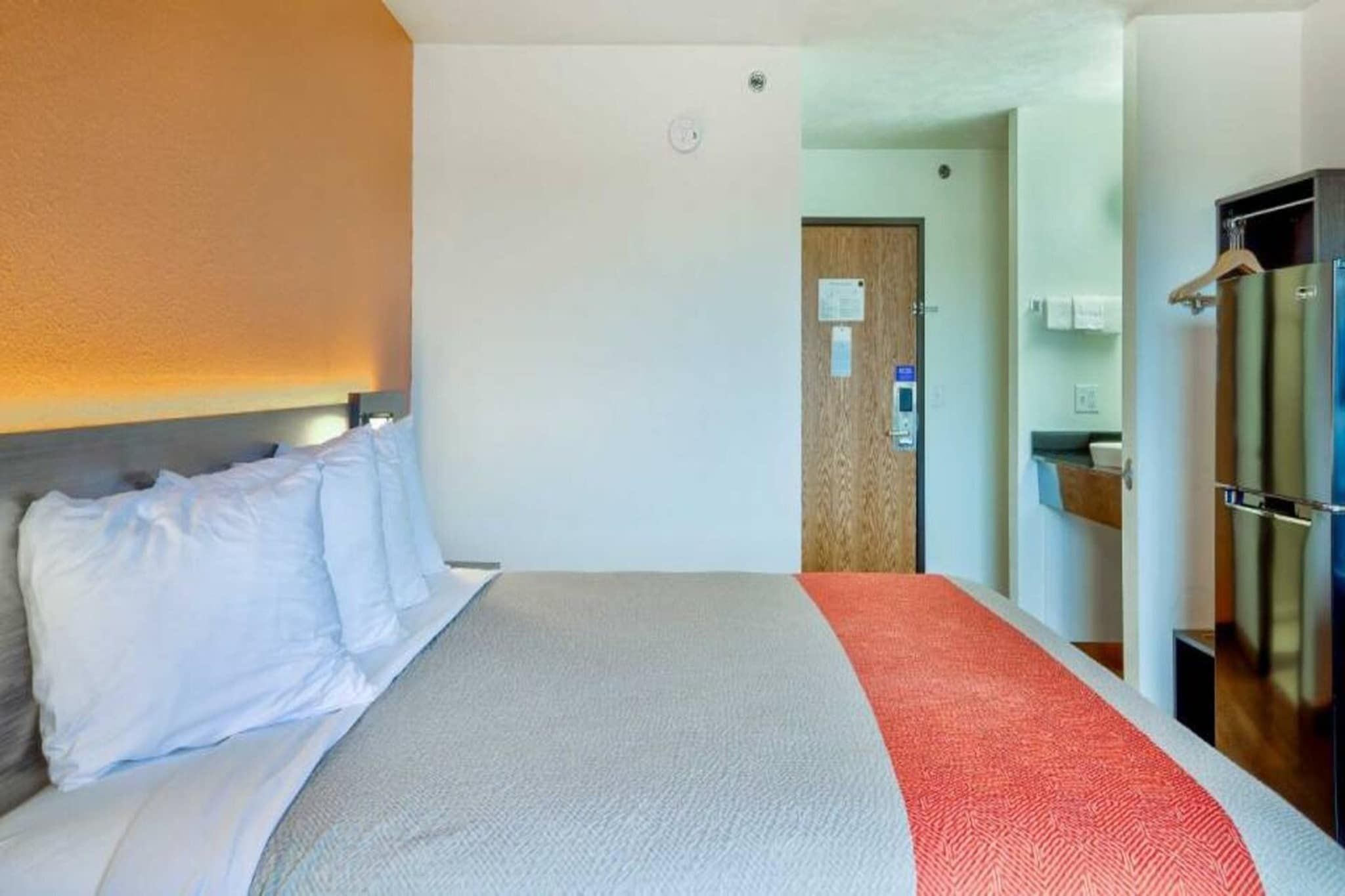 Ein Hotelzimmer mit Bett, einer Tür, einem Spiegel und einer kleinen Küchenzeile.