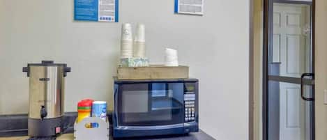 A kitchenette with a coffee maker, microwave, and stacked paper cups.