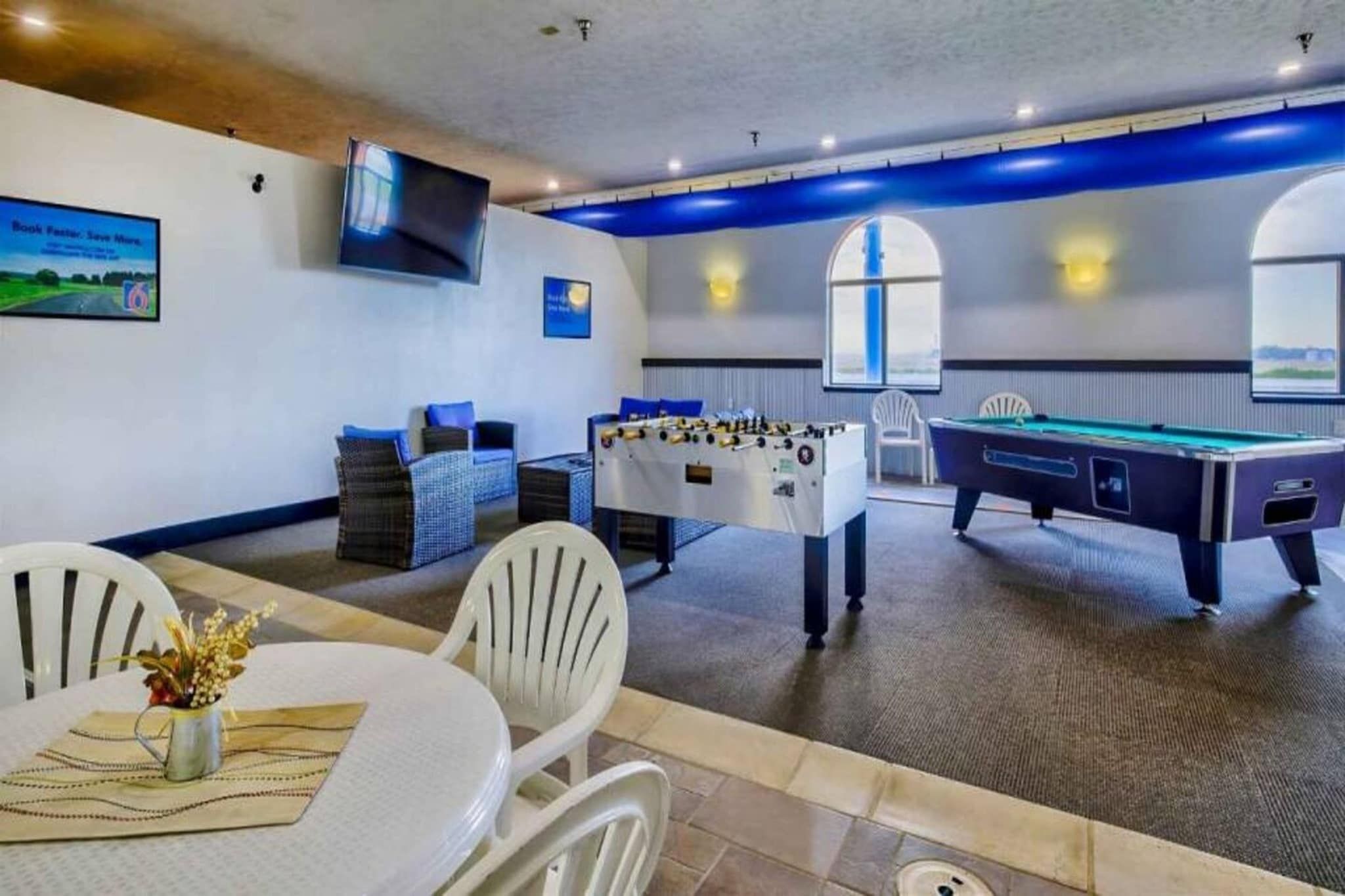 Une pièce équipée d’une table de billard, d’un baby-foot et d’une table avec des chaises et un vase de fleurs.