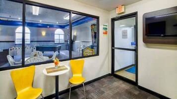 A room with a pool table, two yellow chairs, a small table with a vase, and a large window.