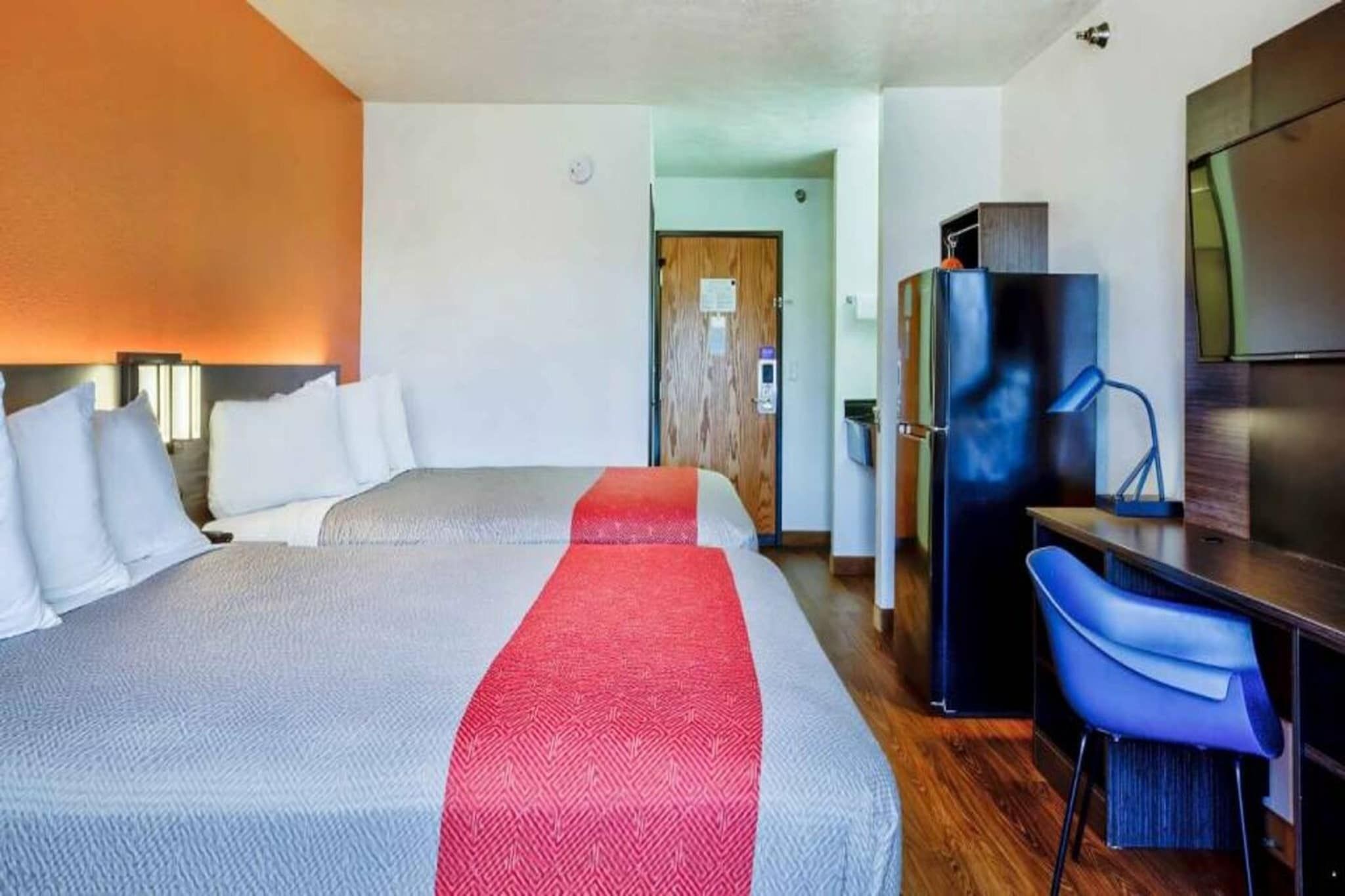 Une chambre d’hôtel avec deux lits, un bureau, une chaise, un réfrigérateur et une télévision.