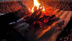 A fire burning in a stone-lined outdoor area with a dog lying nearby.