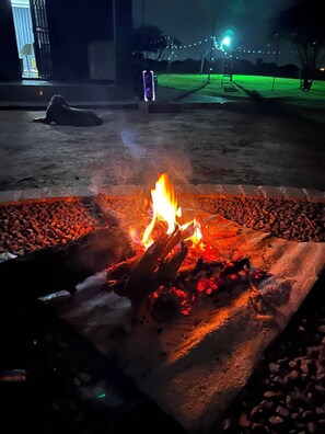 A fire burning in a stone-lined outdoor area with a dog lying nearby.