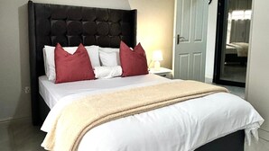 A hotel room with a large bed, a dark headboard, and a bedside lamp.