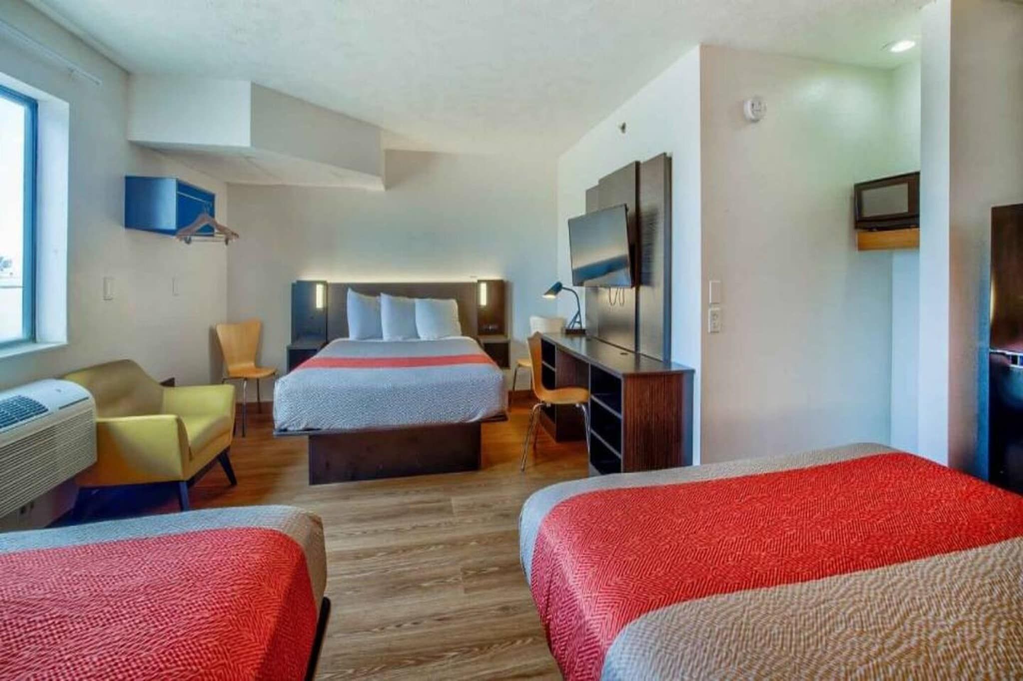 A hotel room with two beds, a desk, a chair, a TV, and a window.