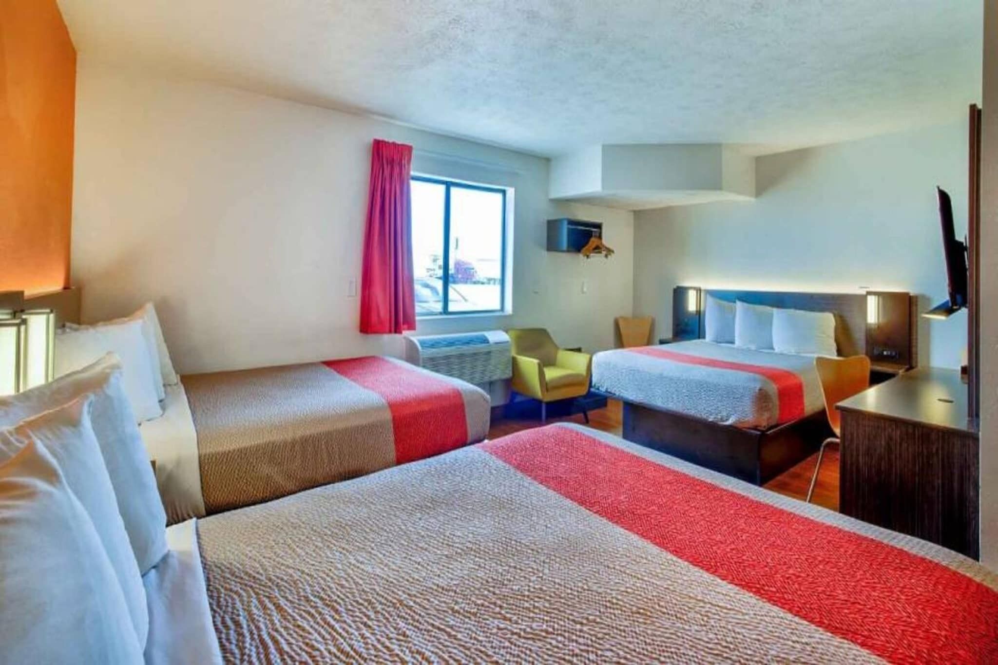 A hotel room with two beds, a TV, a chair, and a window.