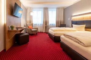 A hotel room with a large bed, a desk, a chair, a TV, and a red carpet. - Hotel Vollmann (Weilheim in Oberbayern)
