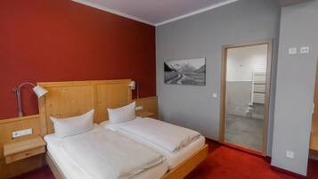 A double bed with a wooden headboard, a bedside table, a wall-mounted lamp, and a picture of a mountainous road.