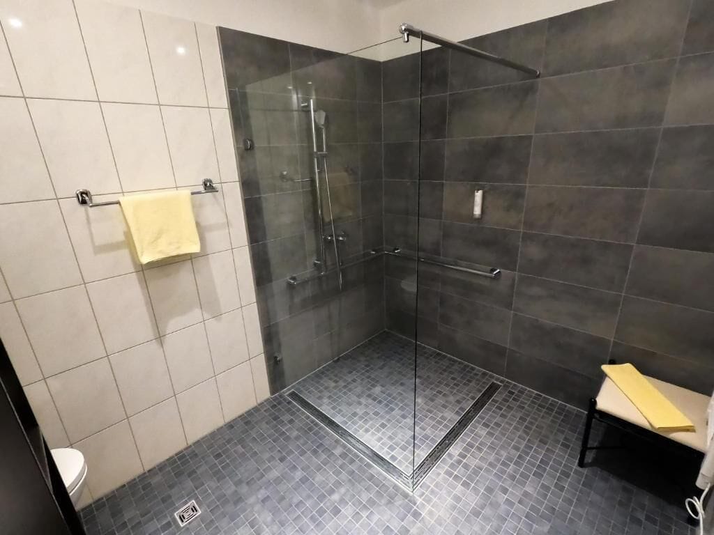 Un baño moderno con ducha envuelta en vidrio, inodoro y un banco.