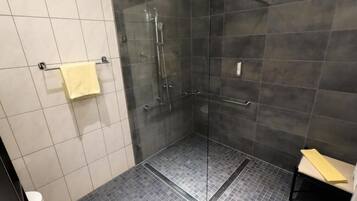Un baño moderno con ducha envuelta en vidrio, inodoro y un banco.