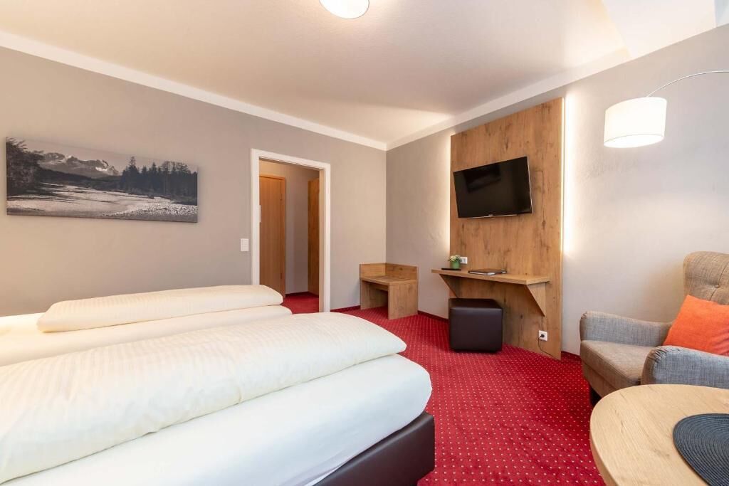 Habitación de hotel con cama, televisión montada en la pared, una mesita y una silla.