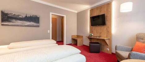 Quarto de hotel com cama, televisão na parede, mesinha e uma cadeira.
