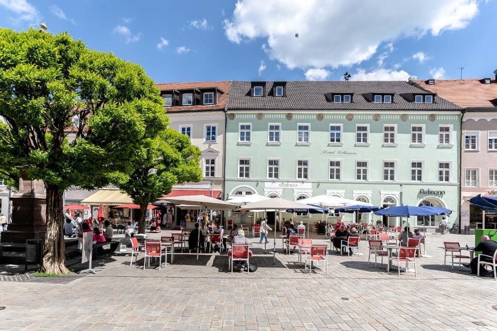 Un patio con mesas al aire libre, un gran árbol y un edificio con un cartel que dice 'Hotel Felsenburg'.