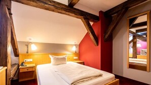 A room with a wooden bed, two bedside tables, a red accent wall, and a mirror.