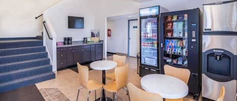Un'area hall di un hotel con una scalinata, angolo cottura, distributori automatici e posti a sedere.