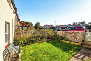 A residential backyard with a stone wall, a grassy lawn, and a parked car. - Berwick - Sleeps 5 -Dogs Stay Free-Enclosed Garden (Berwick-upon-Tweed)