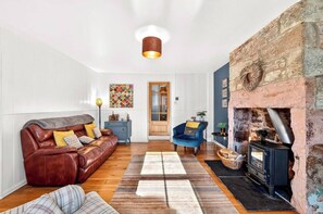 A cozy living room with a leather sofa, a blue armchair, and a stone fireplace. - Berwick - Sleeps 5 -Dogs Stay Free-Enclosed Garden (Berwick-upon-Tweed)
