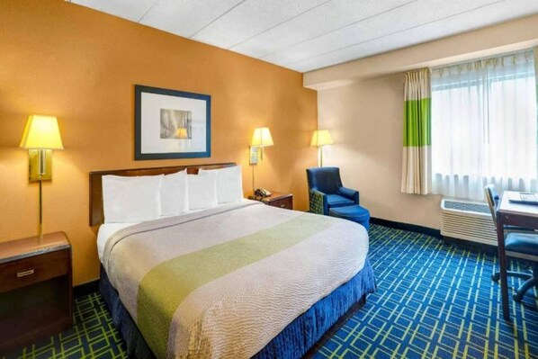 A hotel room with a bed, two bedside lamps, a chair, a desk with a laptop, and a window with curtains.