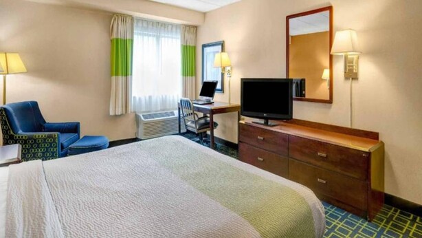 Ein Hotelzimmer mit Bett, Schreibtisch, Stuhl, Fernseher und Kommode.