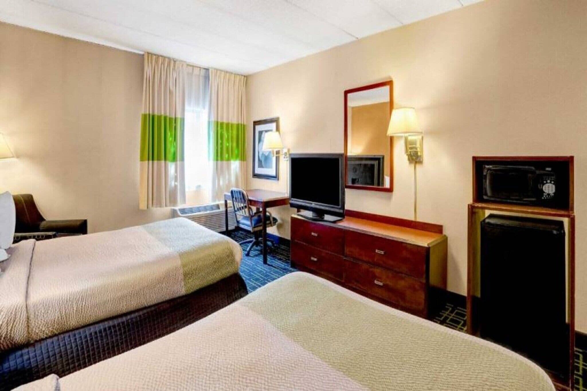 Una habitación de hotel con dos camas, un escritorio, un televisor, un aparador y un microondas.