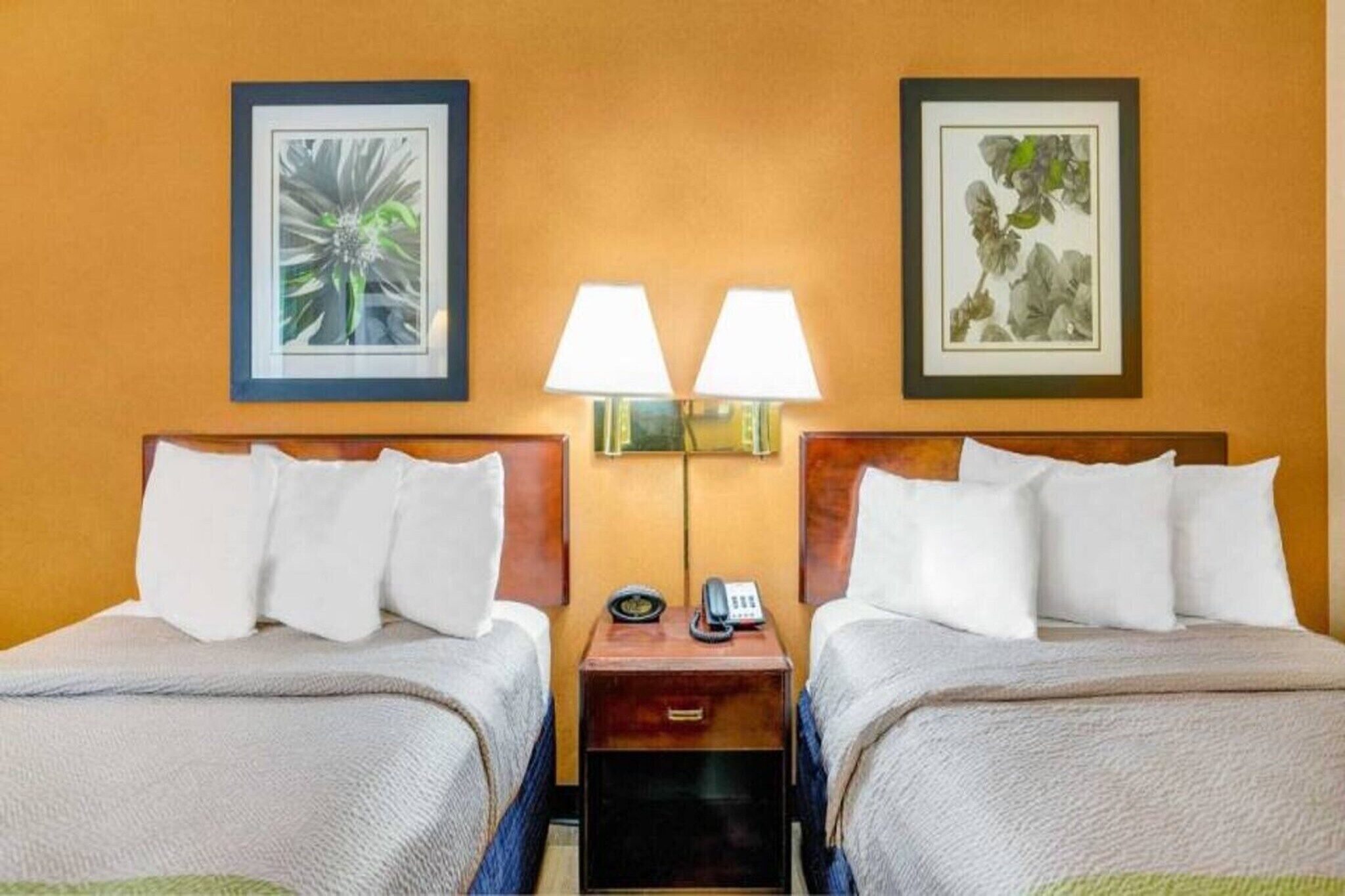 A hotel room with two beds, a nightstand with a phone, and two wall-mounted lamps.
