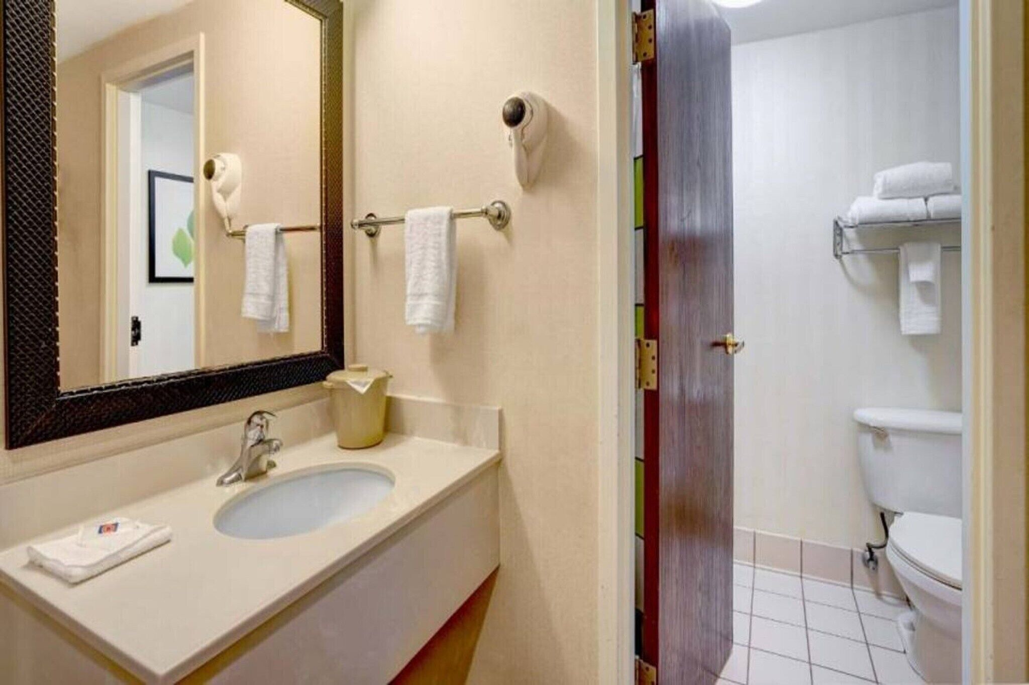 Un baño de hotel con lavamanos, espejo, toallero y retrete.