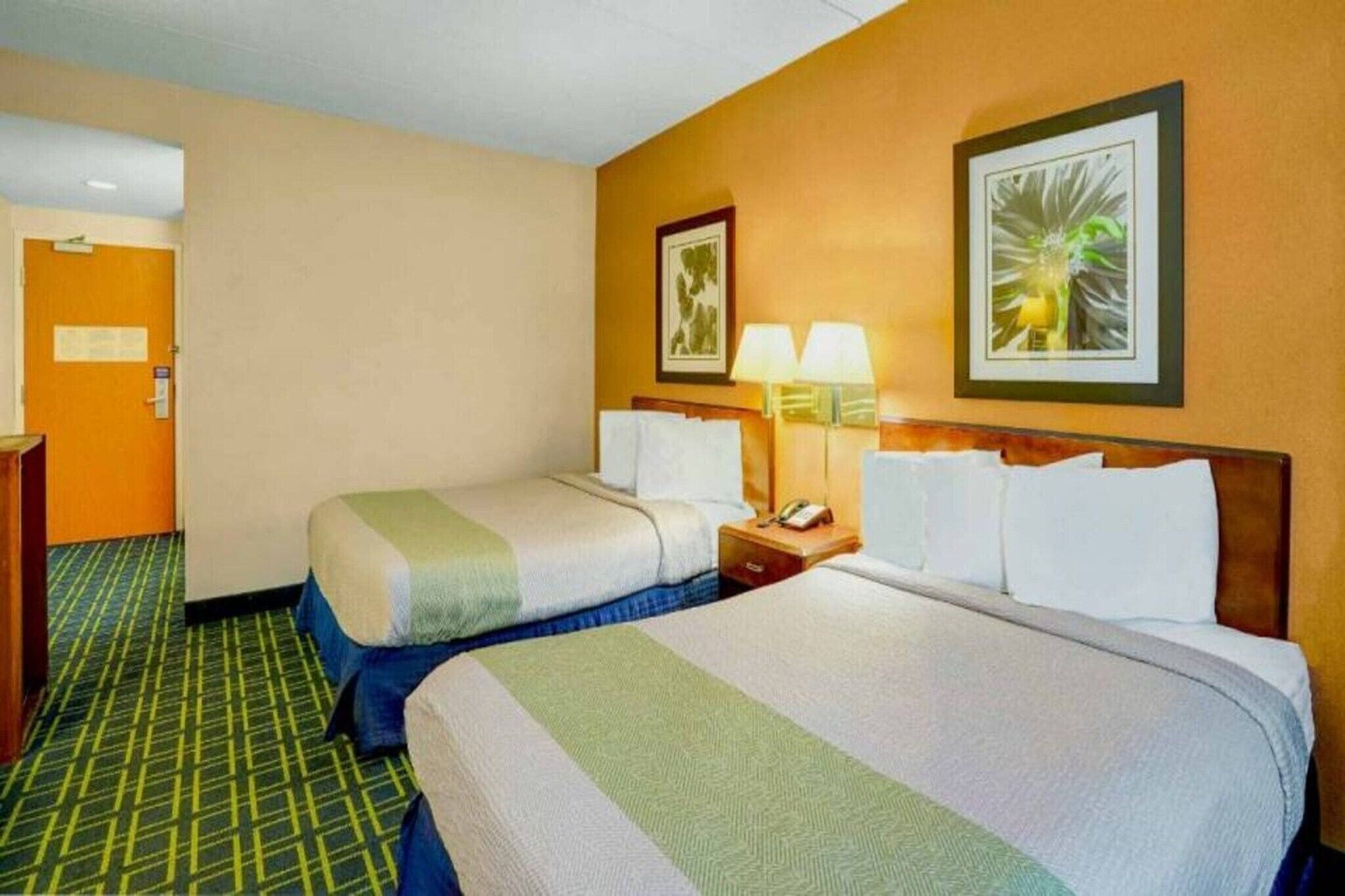 Une chambre d’hôtel avec deux lits, une table de chevet avec une lampe et une porte sur le côté gauche.