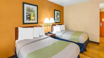Habitación de hotel con dos camas, una mesita de noche con lámpara y cuadros en las paredes.