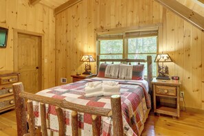 A wooden cabin bedroom with a bed, two nightstands, a window, and a door. - Woolly Bugger Cabin: Hot Tub & Fishing Pond (Blue Ridge)