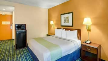 Una habitación de hotel con cama, escritorio, teléfono, lámpara y refrigerador.
