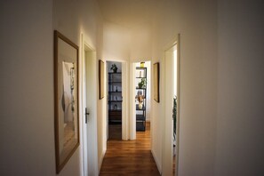 Ein Korridor mit Holzboden, gerahmten Kunstwerken an den Wänden und einer Tür zu einem Raum mit Regalen.