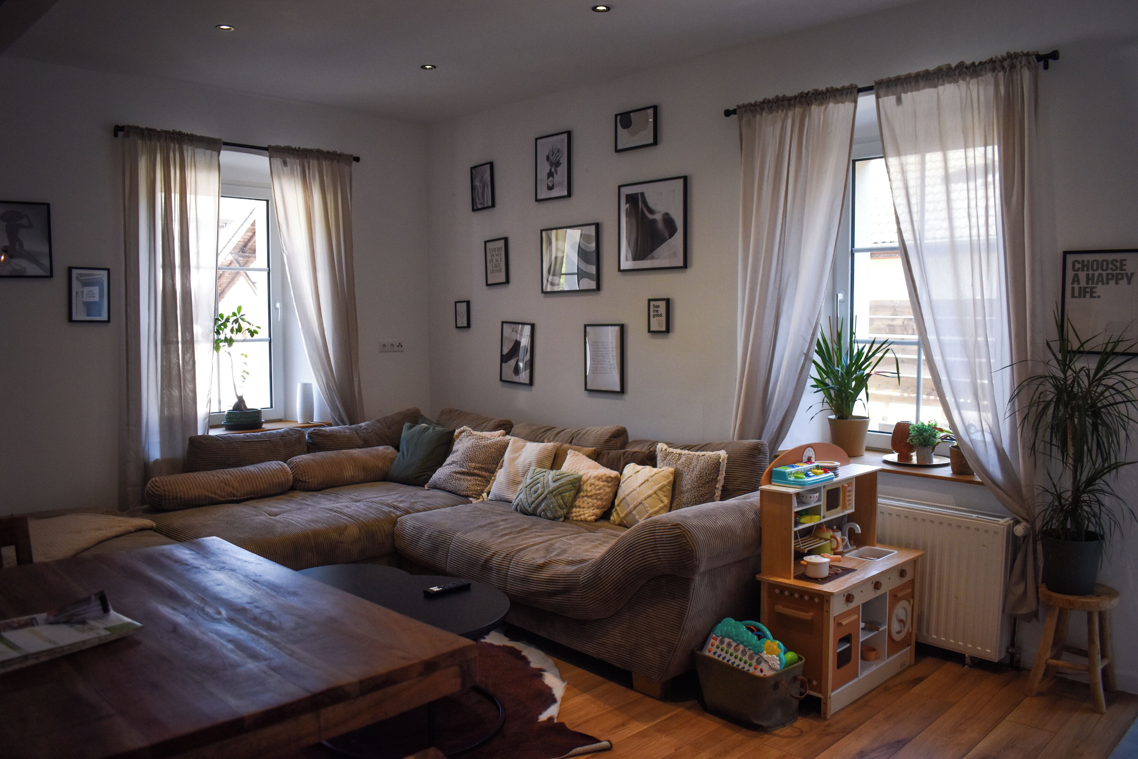 Ein gemütliches Wohnzimmer mit einer Eckcouch, einem Holztisch und einem Spielbereich für Kinder mit Spielzeug und einem kleinen Bücherregal.