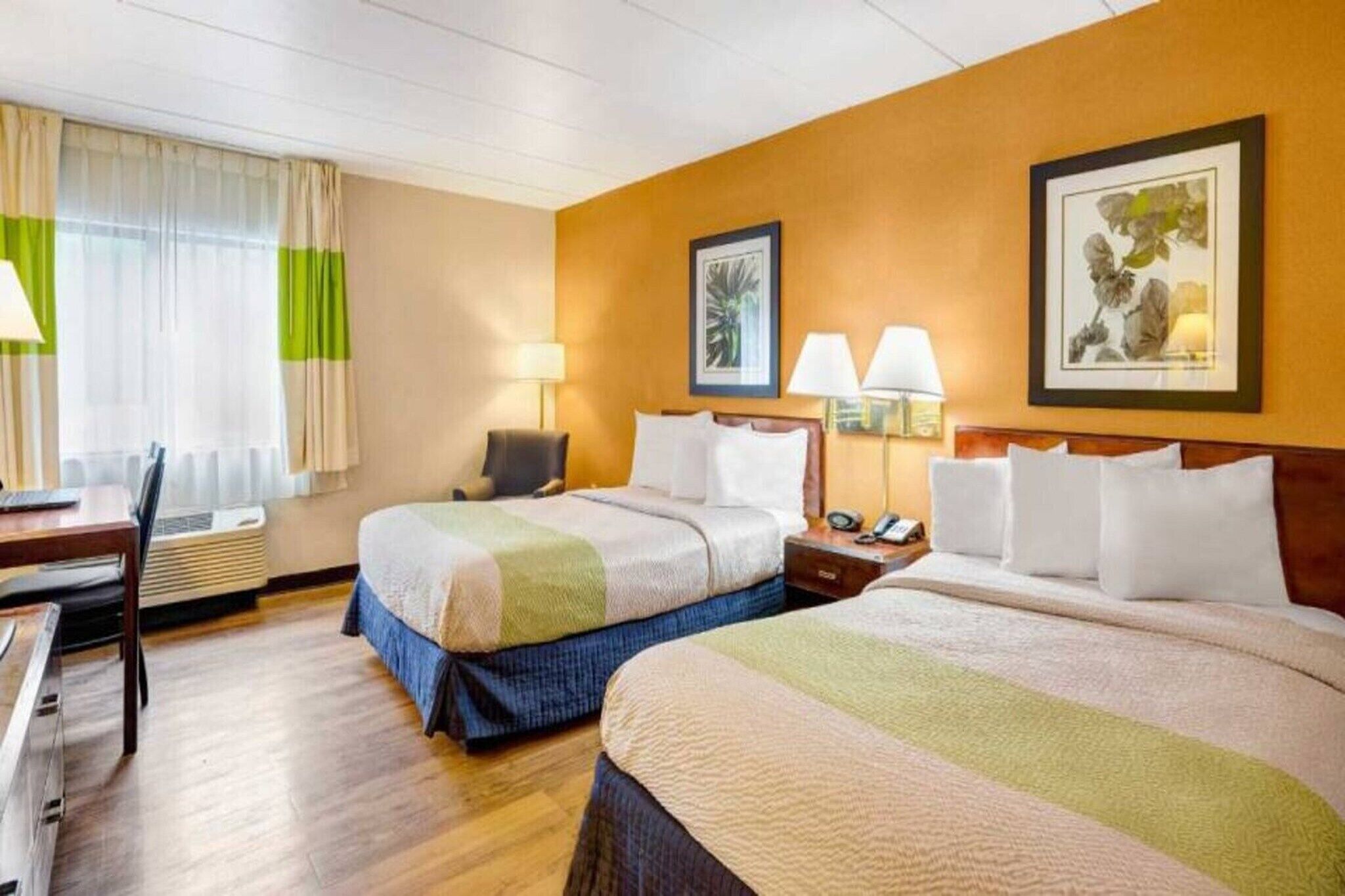 Habitación de hotel con dos camas, un escritorio y una silla. Hay lámparas en el escritorio y mesitas de noche con lámparas junto a cada cama.