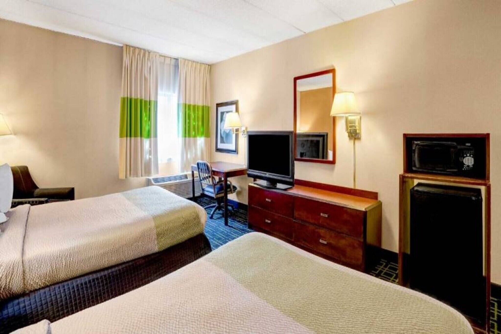 Une chambre d’hôtel avec deux lits, un bureau, une télévision, une commode et un four à micro-ondes.