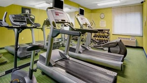 Ein Fitnessraum mit Laufbändern, Crosstrainern und einer Hantelbank.