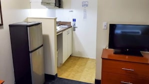 Ett kompakt kök med ett kylskåp, en mikrovågsugn, en diskho och en tv placerad på ett träskåp.