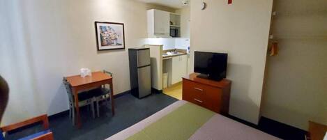 A hotel room with a bed, a desk, a television, a kitchenette, and a small bathroom.