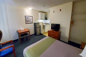 A hotel room with a bed, a desk, a television, a kitchenette, and a small bathroom. - 1 Queen Bed | Smoking (Richmond VA)