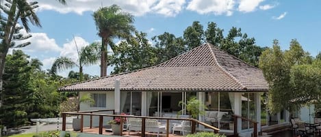 A house with a covered patio, a pool, and lush greenery.