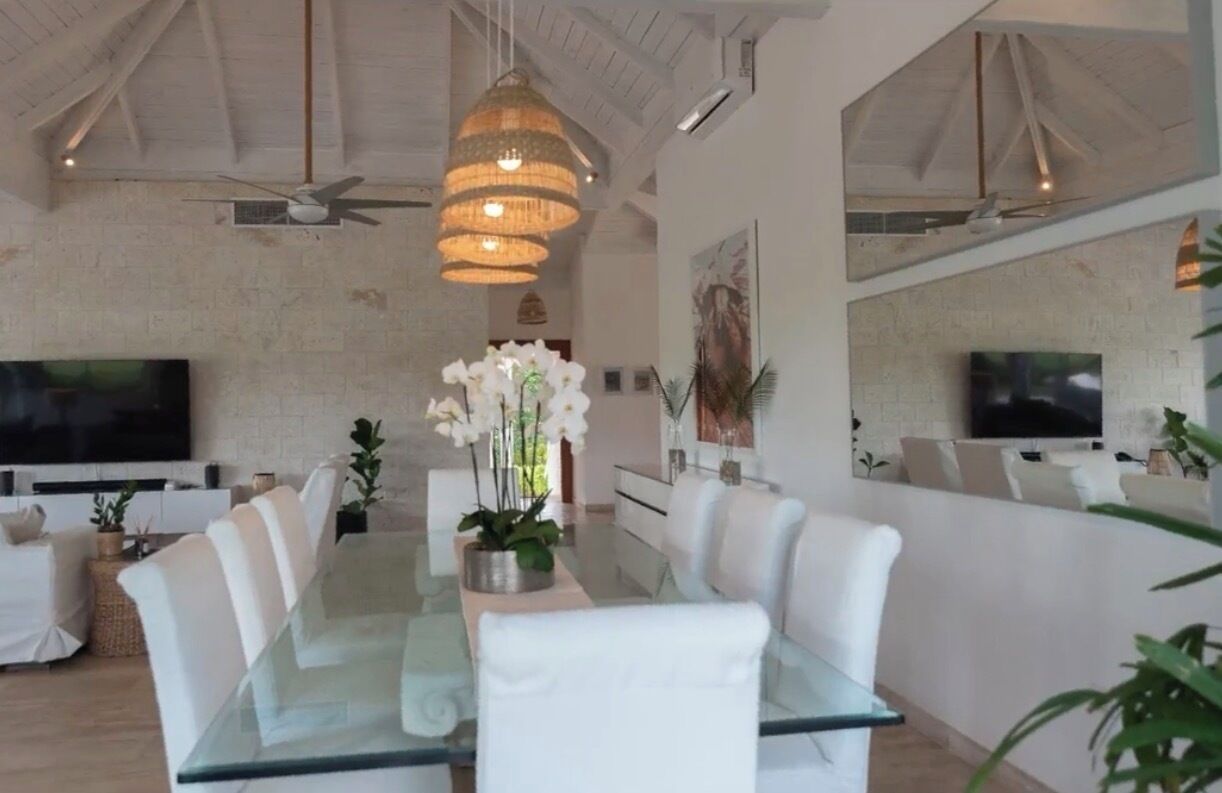 Un comedor moderno con una mesa de vidrio, sillas blancas y un ventilador de techo.