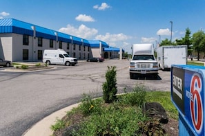 A motel with a blue roof, a parking lot with several vehicles, and a sign indicating the motel's name.