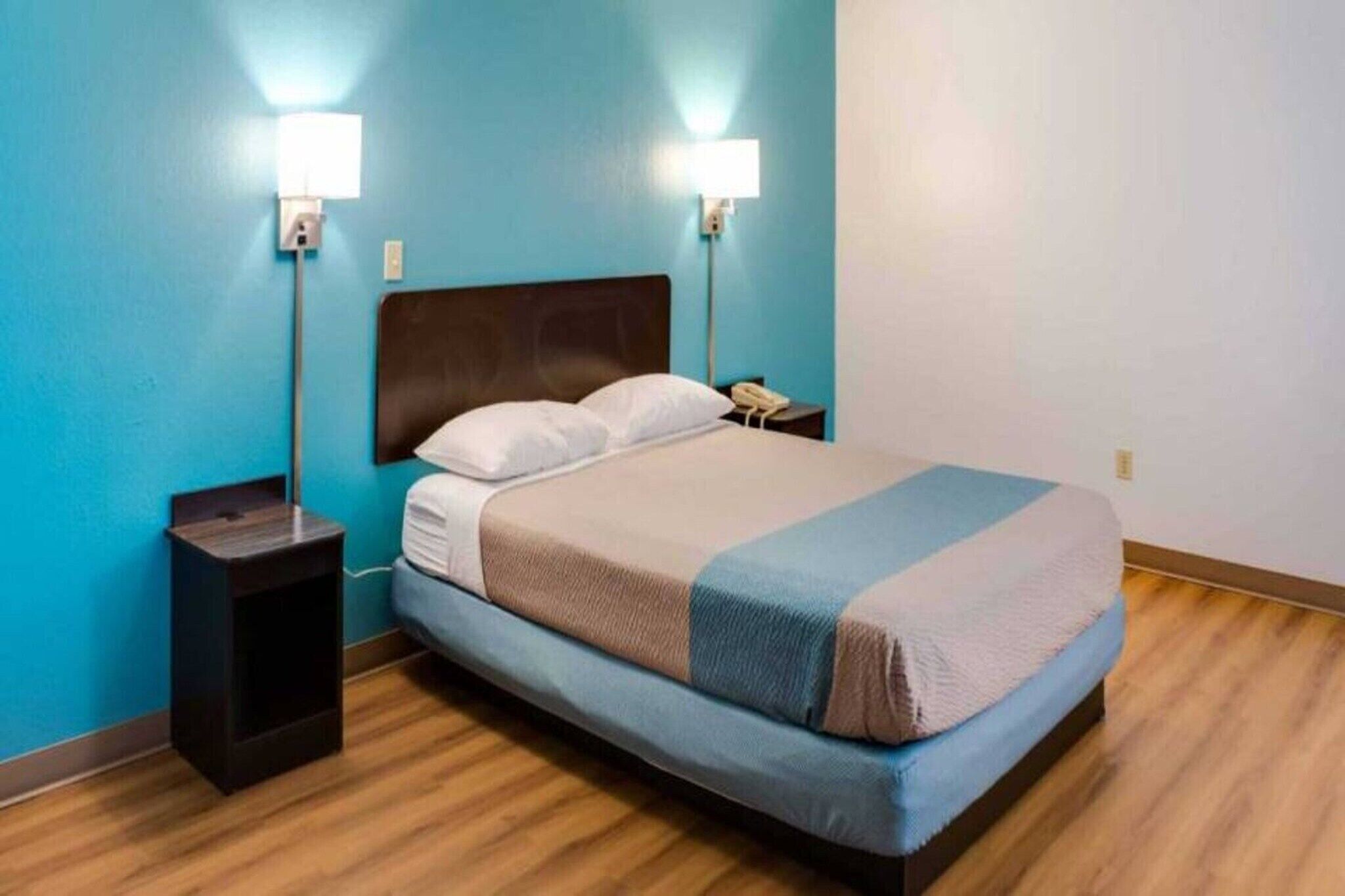 A hotel room with a bed, two bedside lamps, a nightstand, and a phone.
